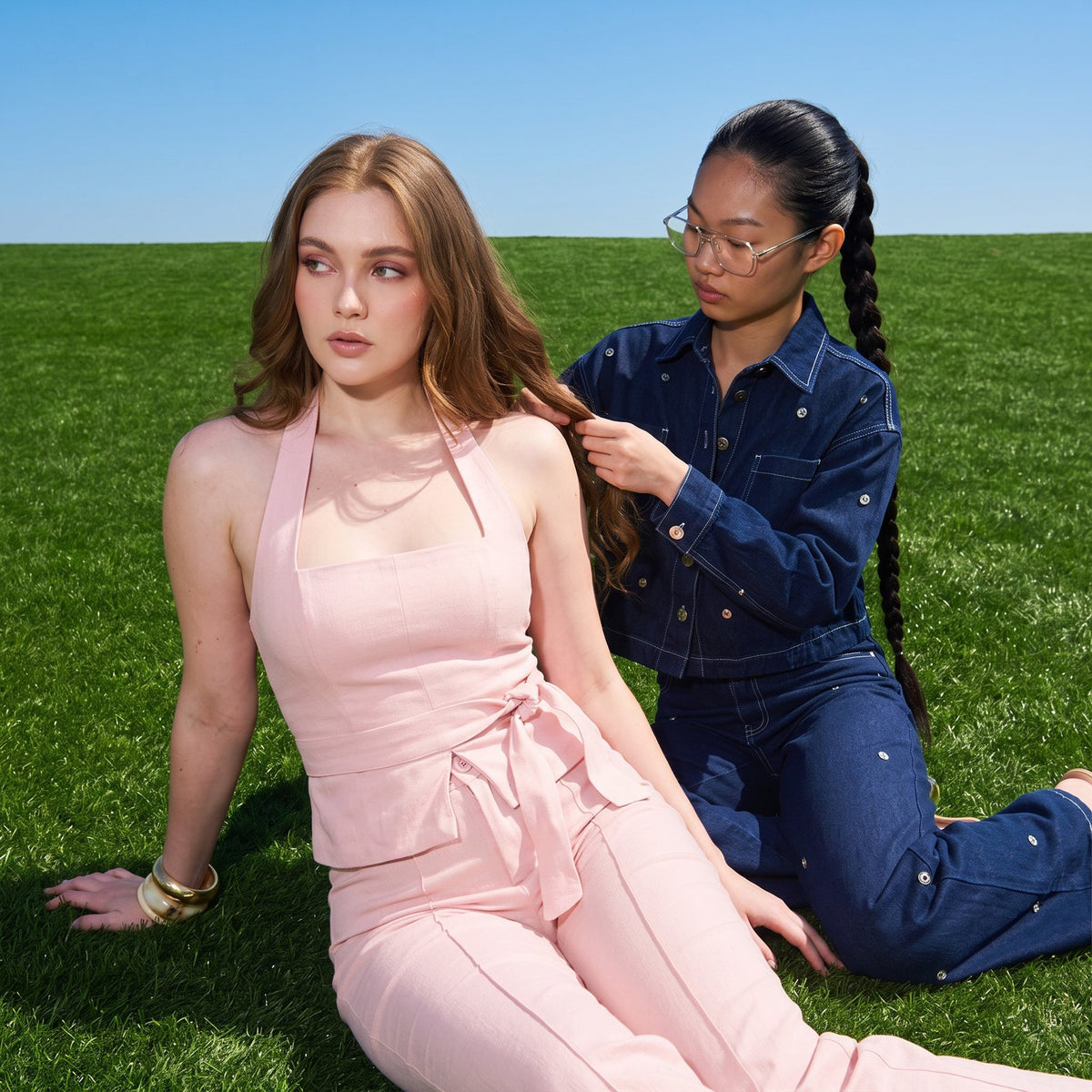 Dos modelos sentadas en el pasto: set rosa y denim con tachas